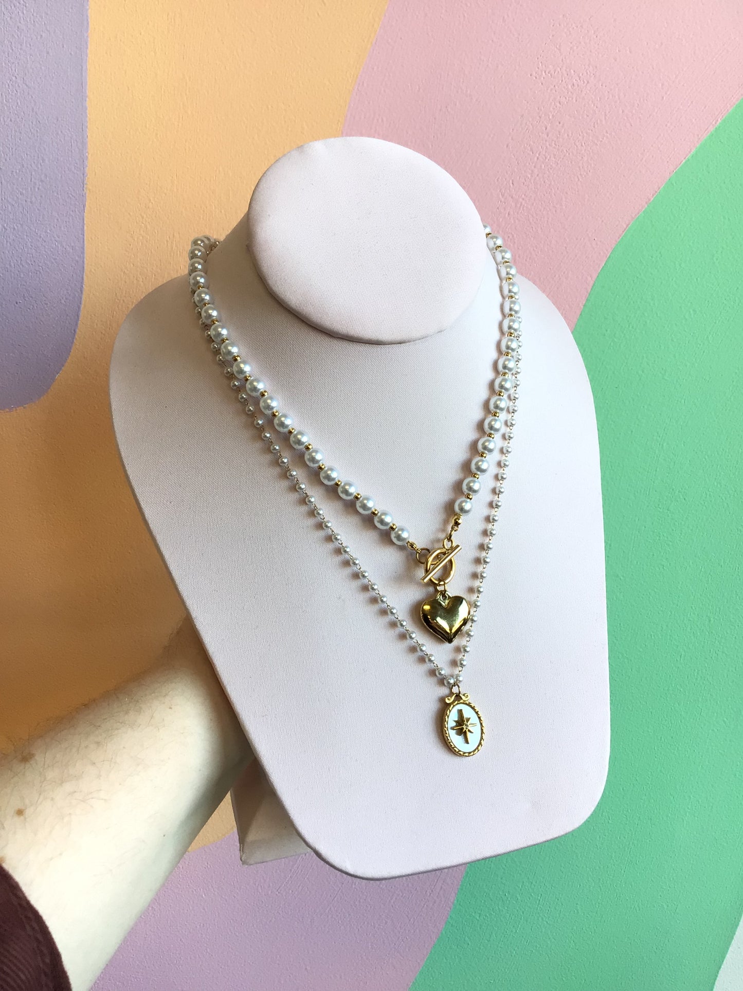 Simply Sweet Front Clasp Necklace shown on product stand in front of wavy colorful background