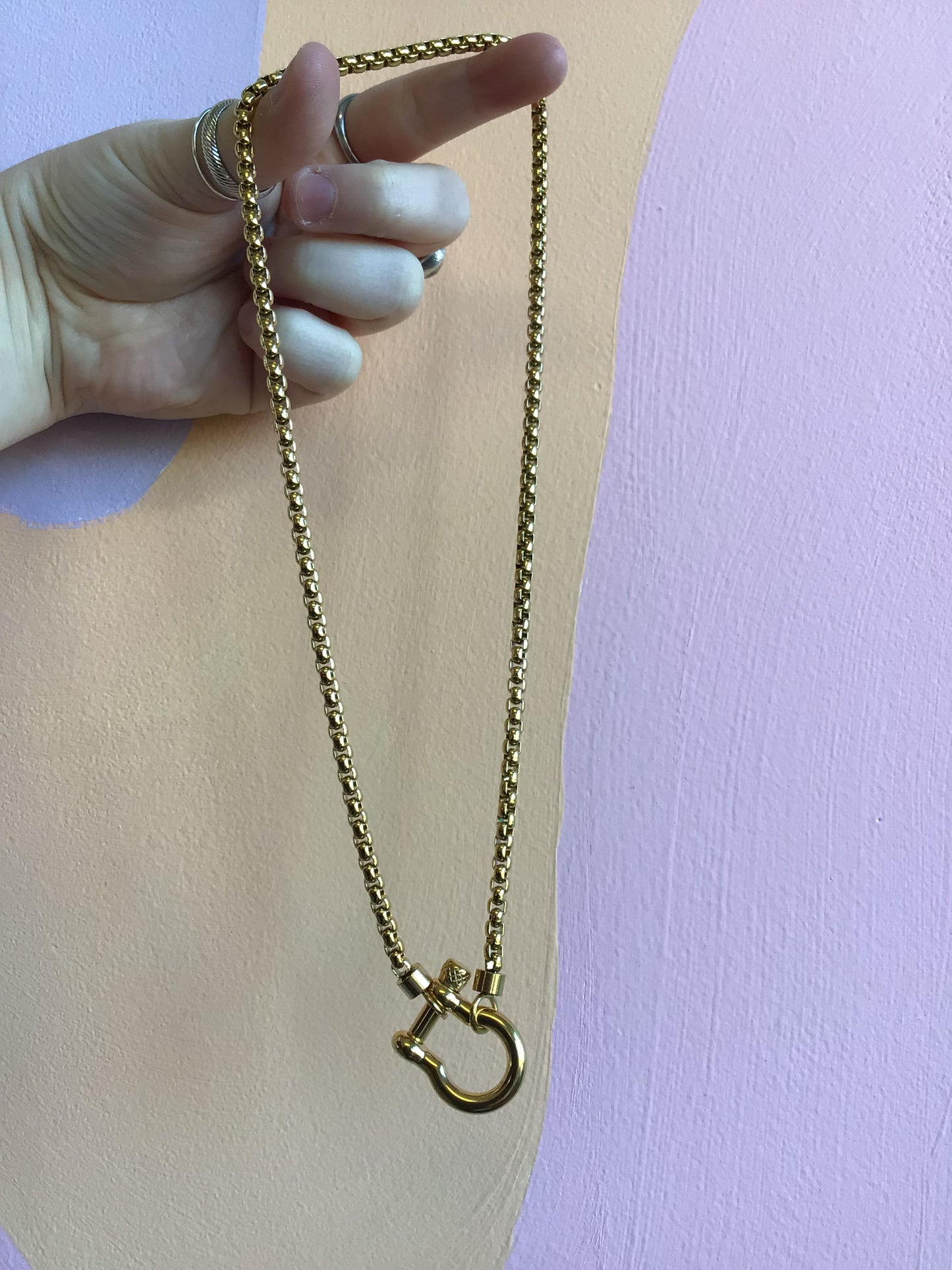 Horseshoe Lock Titanium Necklace in gold held in hand in front of wavy colorful background