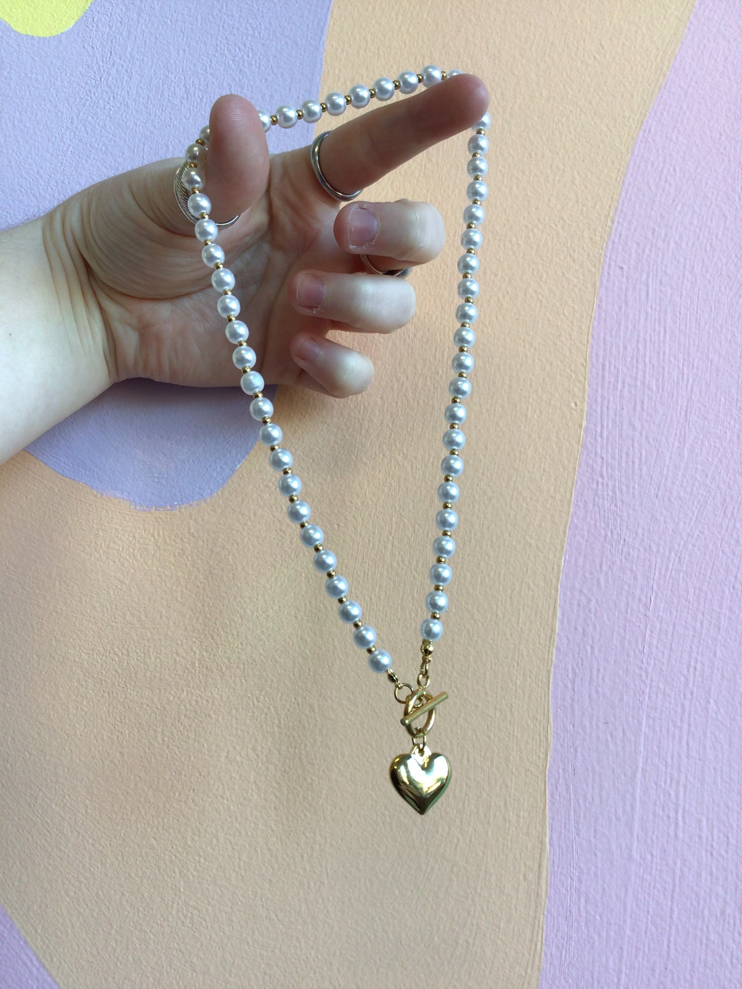 Simply Sweet Front Clasp Necklace in hand in front of wavy colorful background