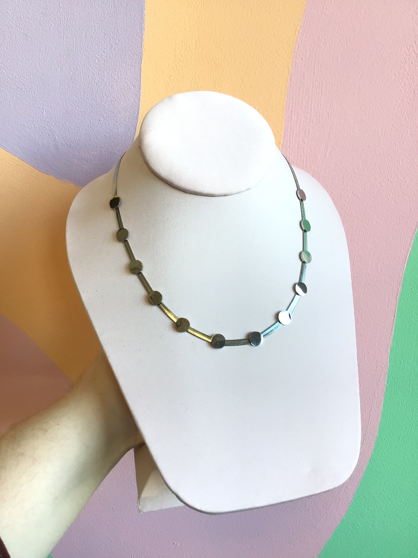 Flat Disc Stacker Titanium Chain in silver shown on product stand in front of wavy colorful background