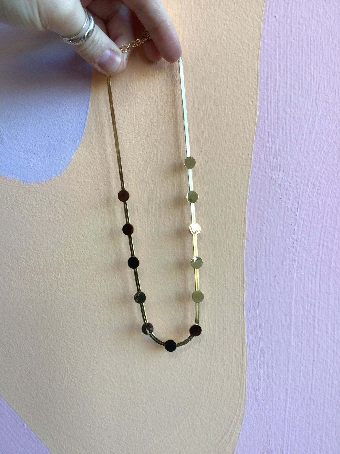 Flat Disc Stacker Titanium Chain in gold held in hand in front of wavy colorful background
