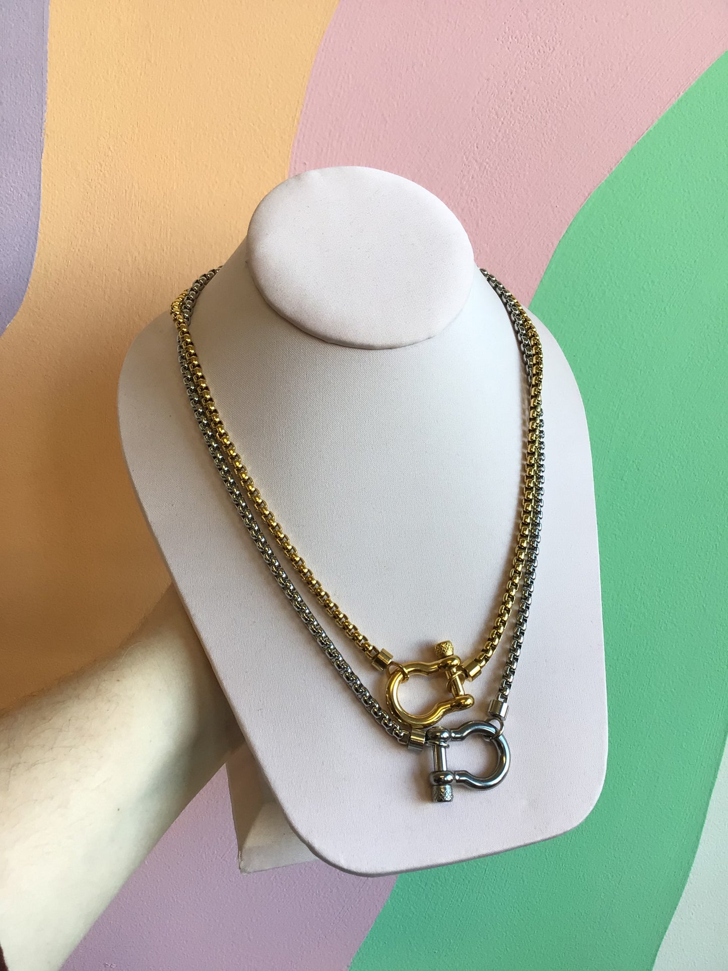 Horseshoe Lock Titanium Necklace in silver and gold shown on product stand in front of wavy colorful background
