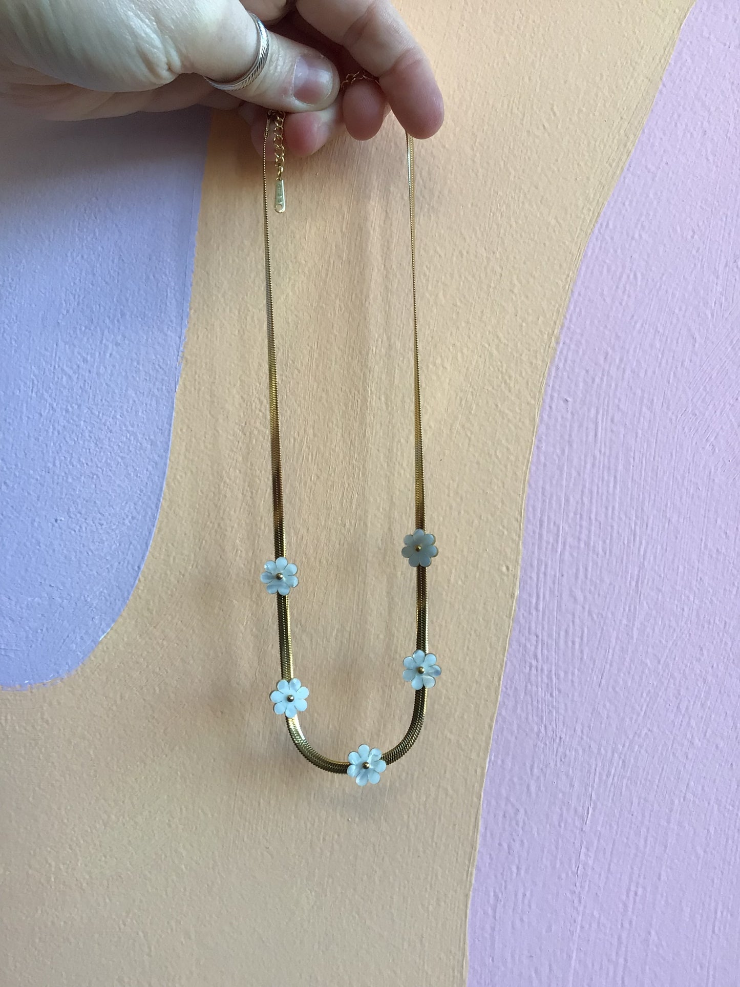 Flat Daisy Titanium Chain held in hand in front of wavy colorful background