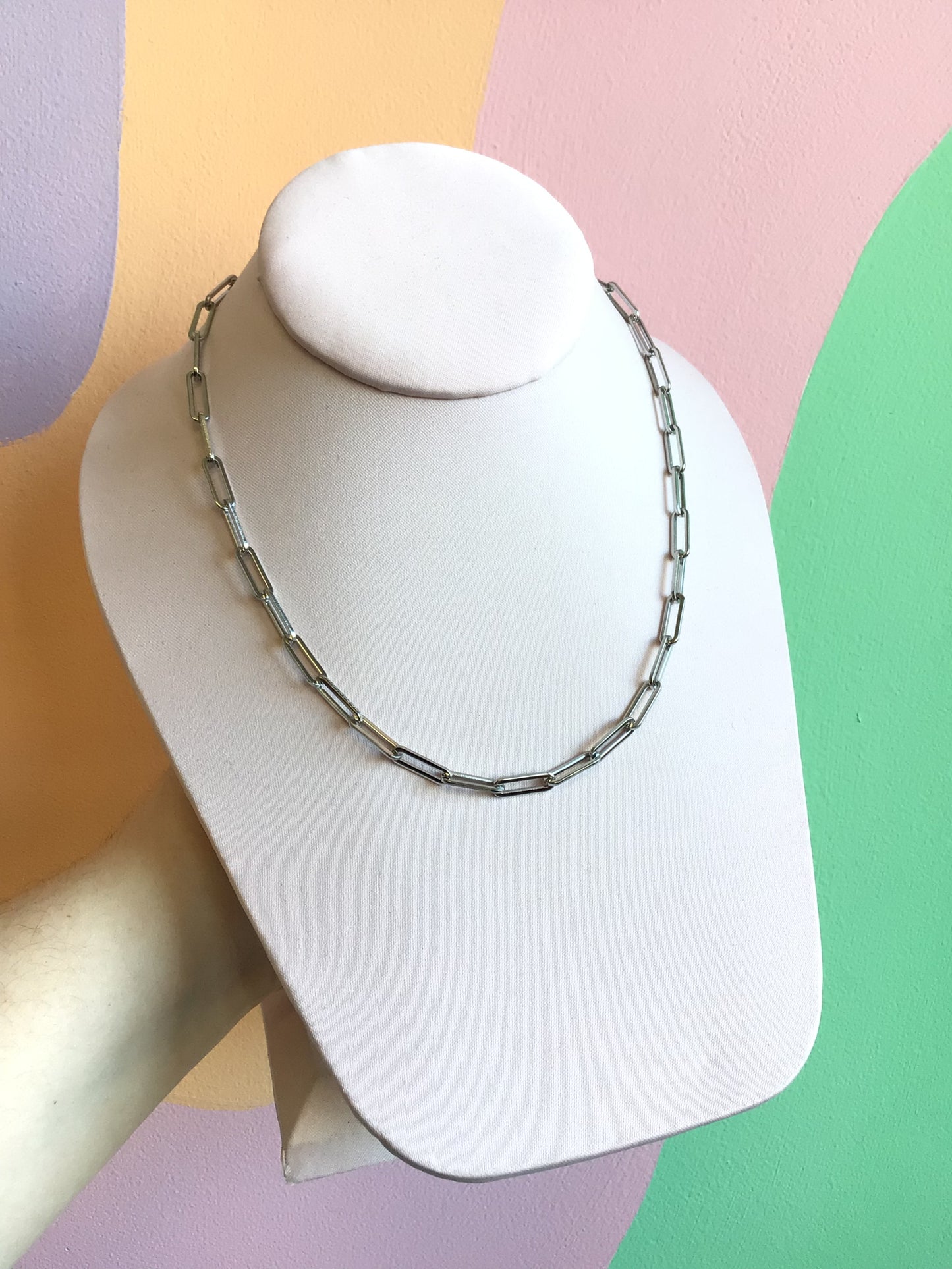Paperclip Chain Necklace shown on product stand in front of wavy colorful background