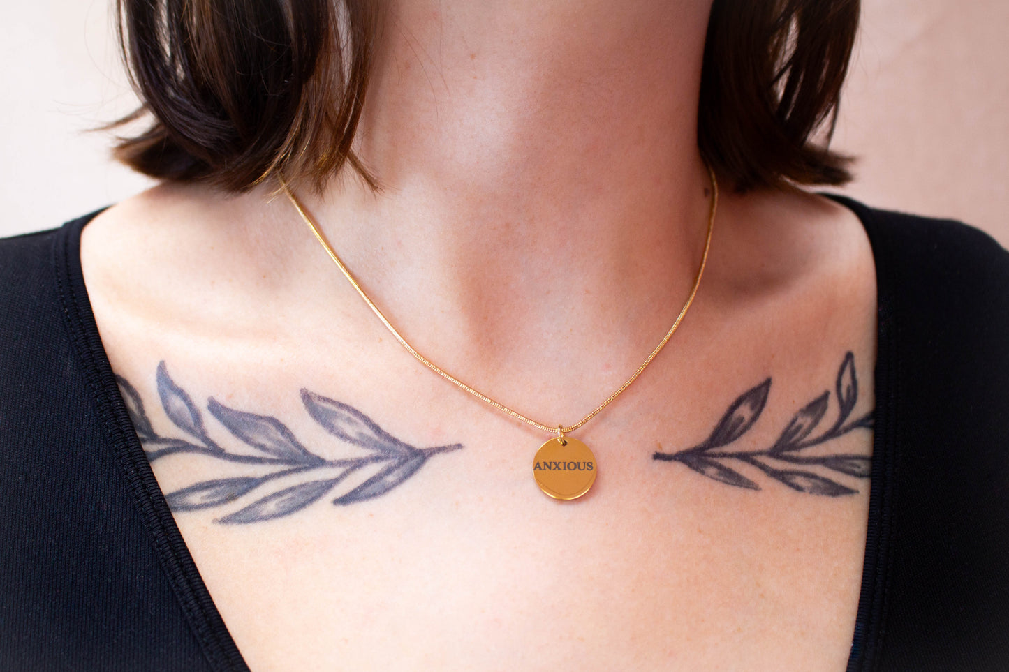 Close up image of round chain and engraved "Anxious" charm around model's neck