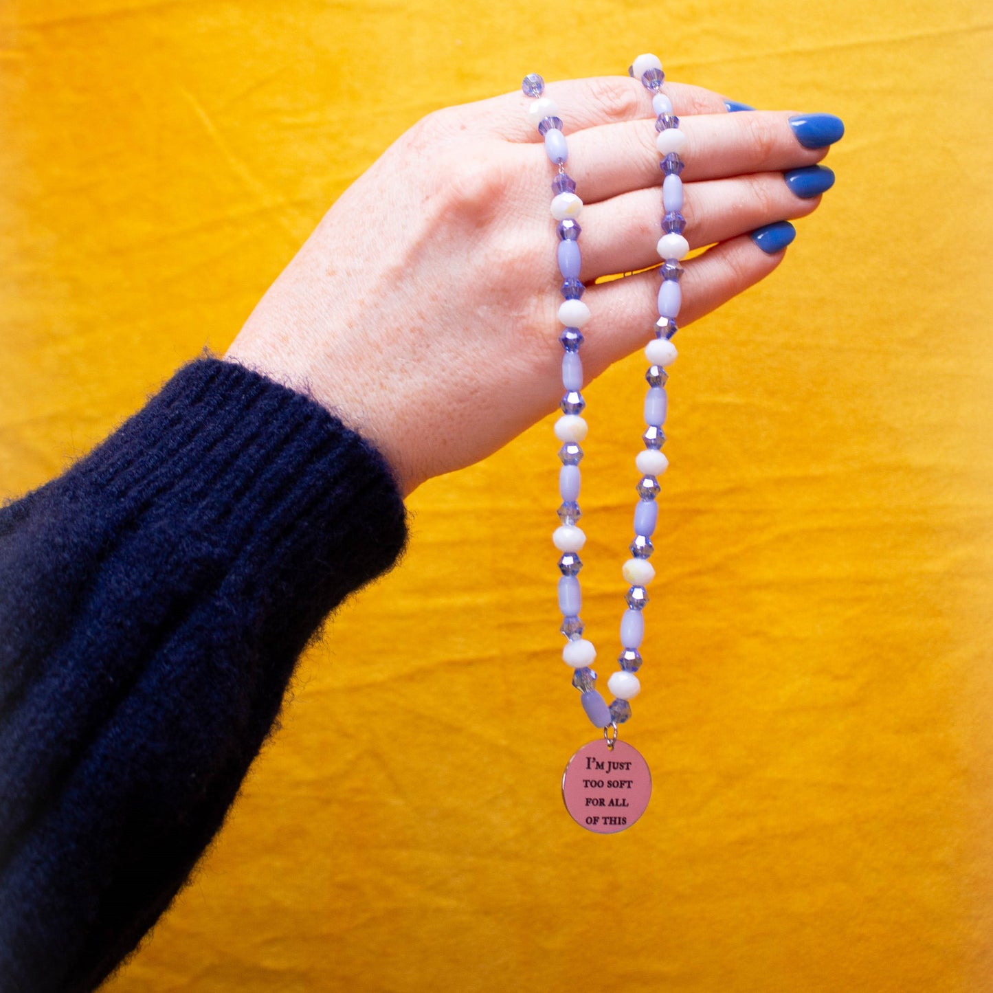 Hand holding beaded and engraved charm necklace in front of yellow backdrop