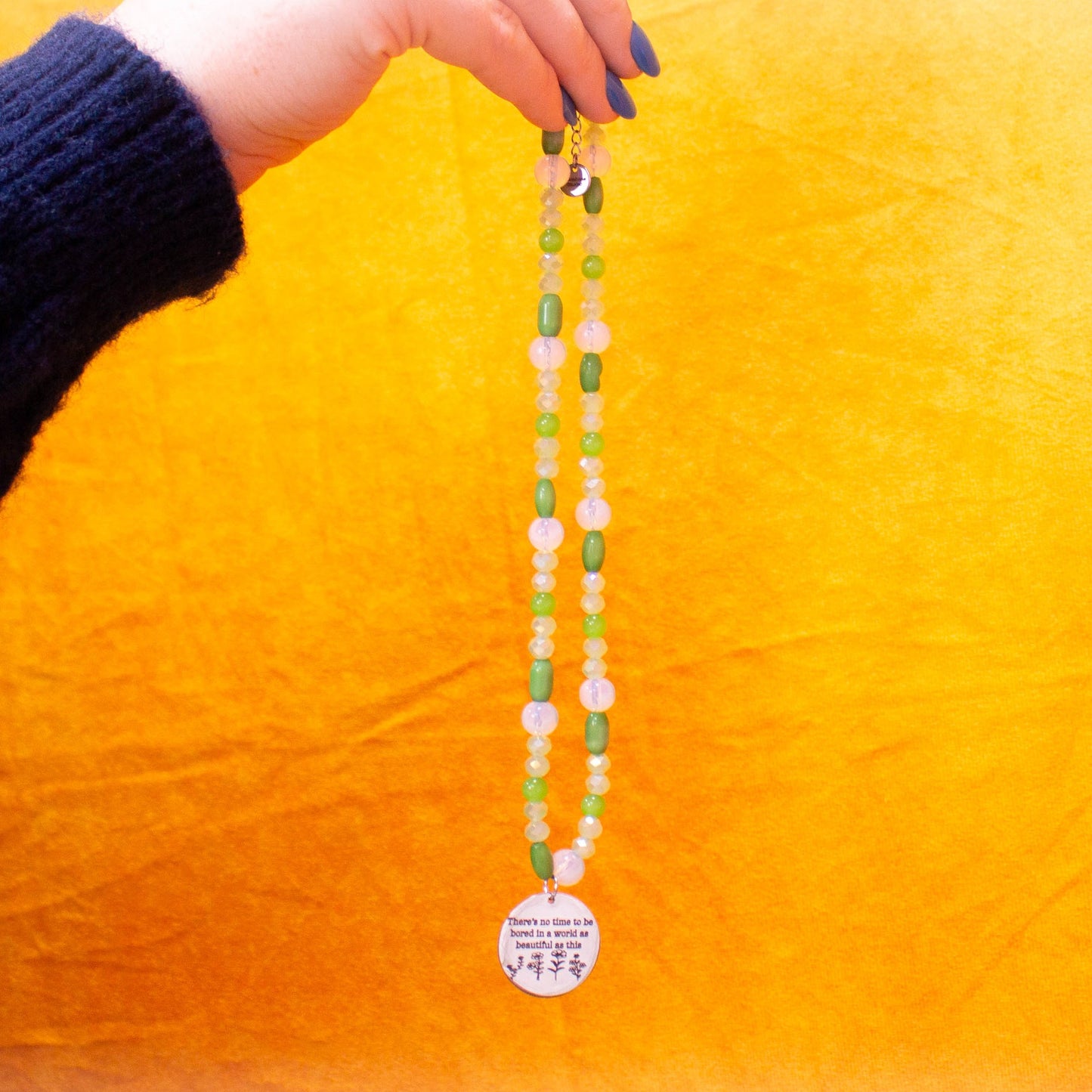 Hand holding beaded and engraved charm necklace in front of yellow backdrop