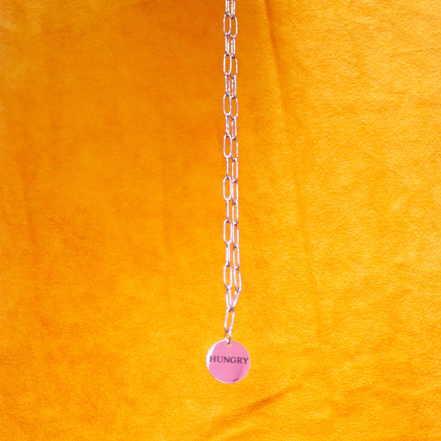 hanging "Hungry" engraved necklace in front of yellow backdrop