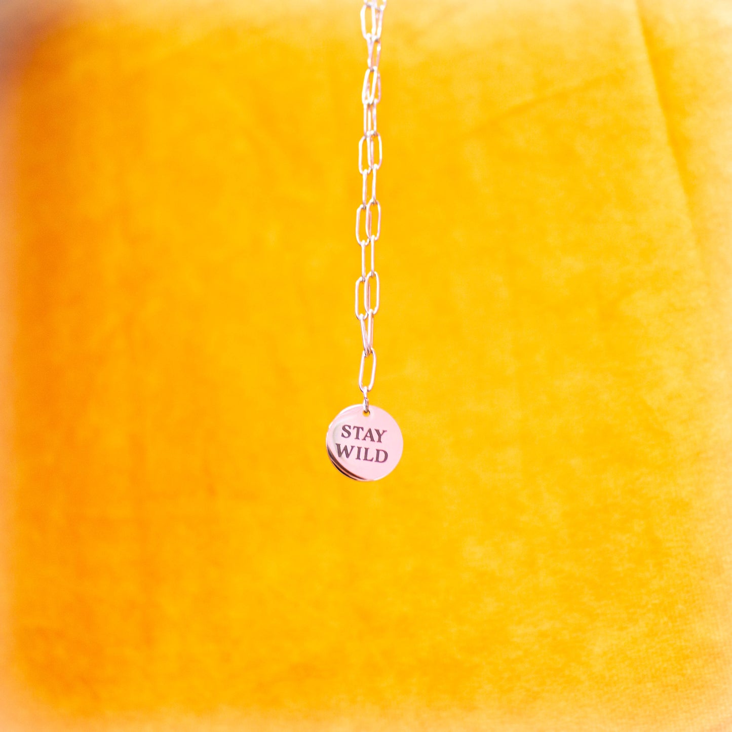 "Stay Wild" engraved charm necklace hanging in front of yellow backdrop