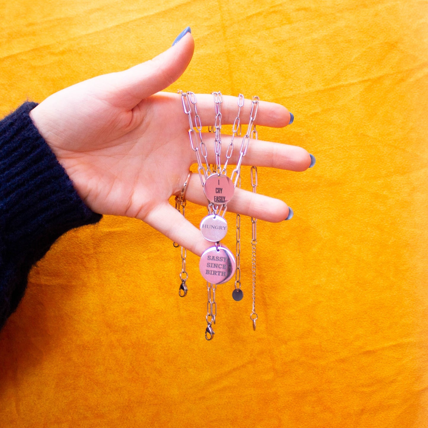 Hand holding multiple engraved charm necklaces in front of yellow backdrop