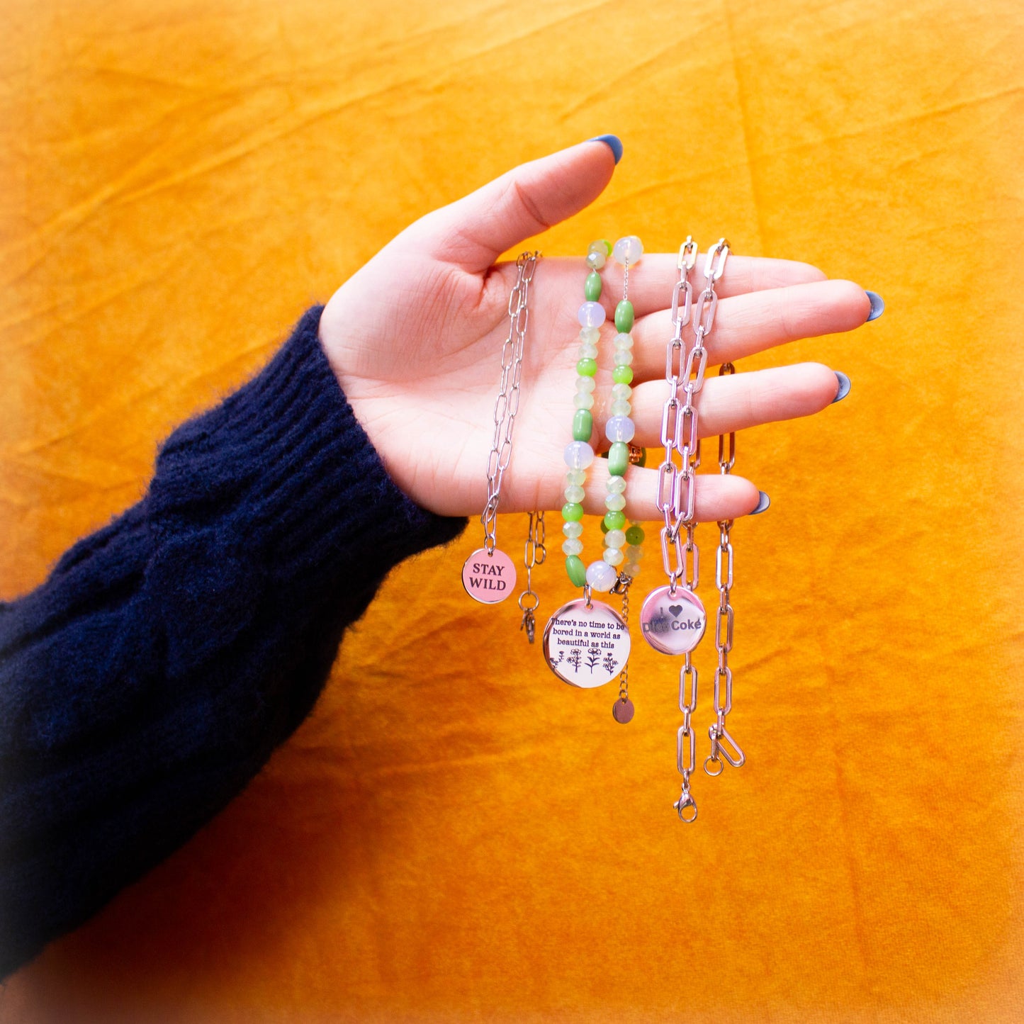 Hand holding multiple engraved charm necklaces in front of yellow backdrop