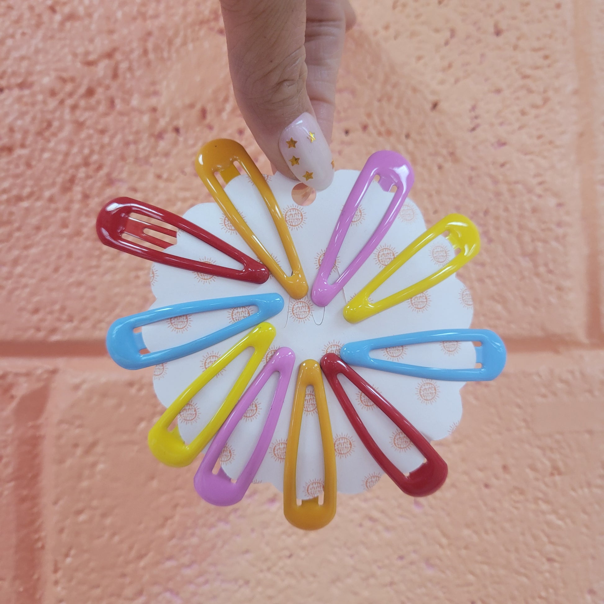 A picture showing 10 colorful enamel coated snap clip barrettes. 2 of each in red, orange, yellow, blue, and lilac.