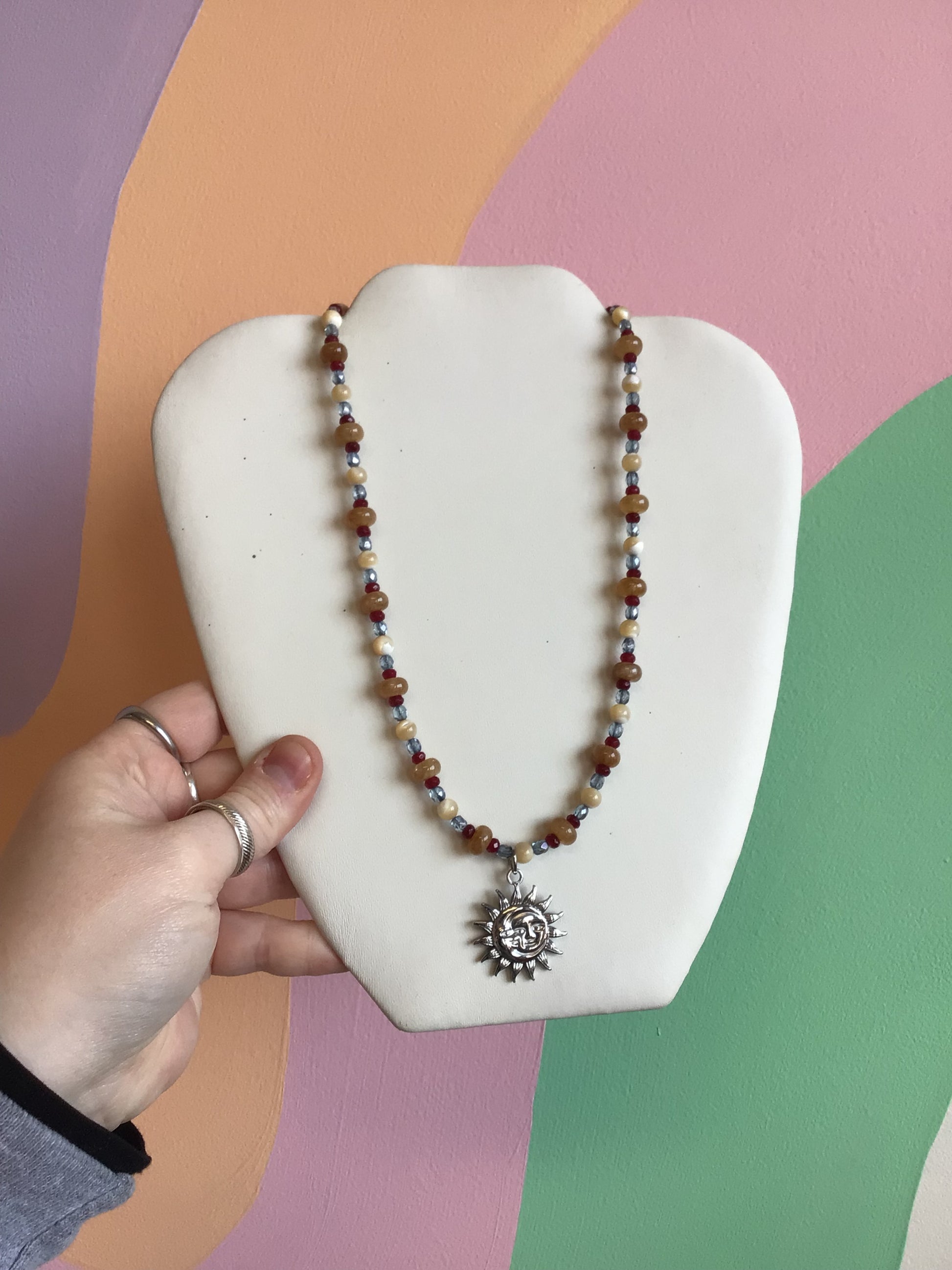 A necklace made up of a pattern of earth-tone brown glass beads ad smaller blue and brown seed beads. A silver titanium charm of a sun and moon is hanging from the middle.