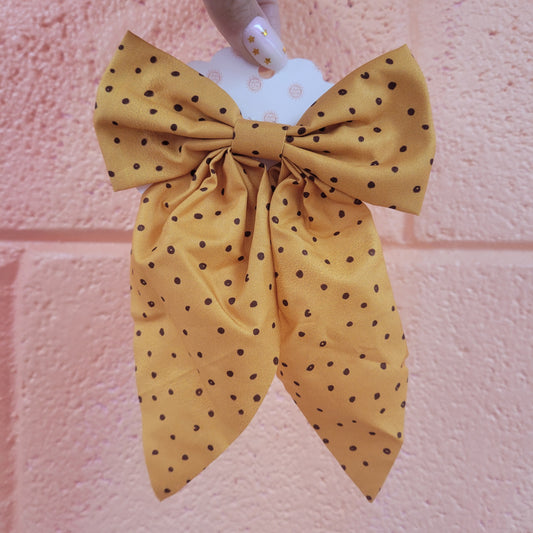 An amber yellow hair bow clip with small, brown polka dots throughout.
